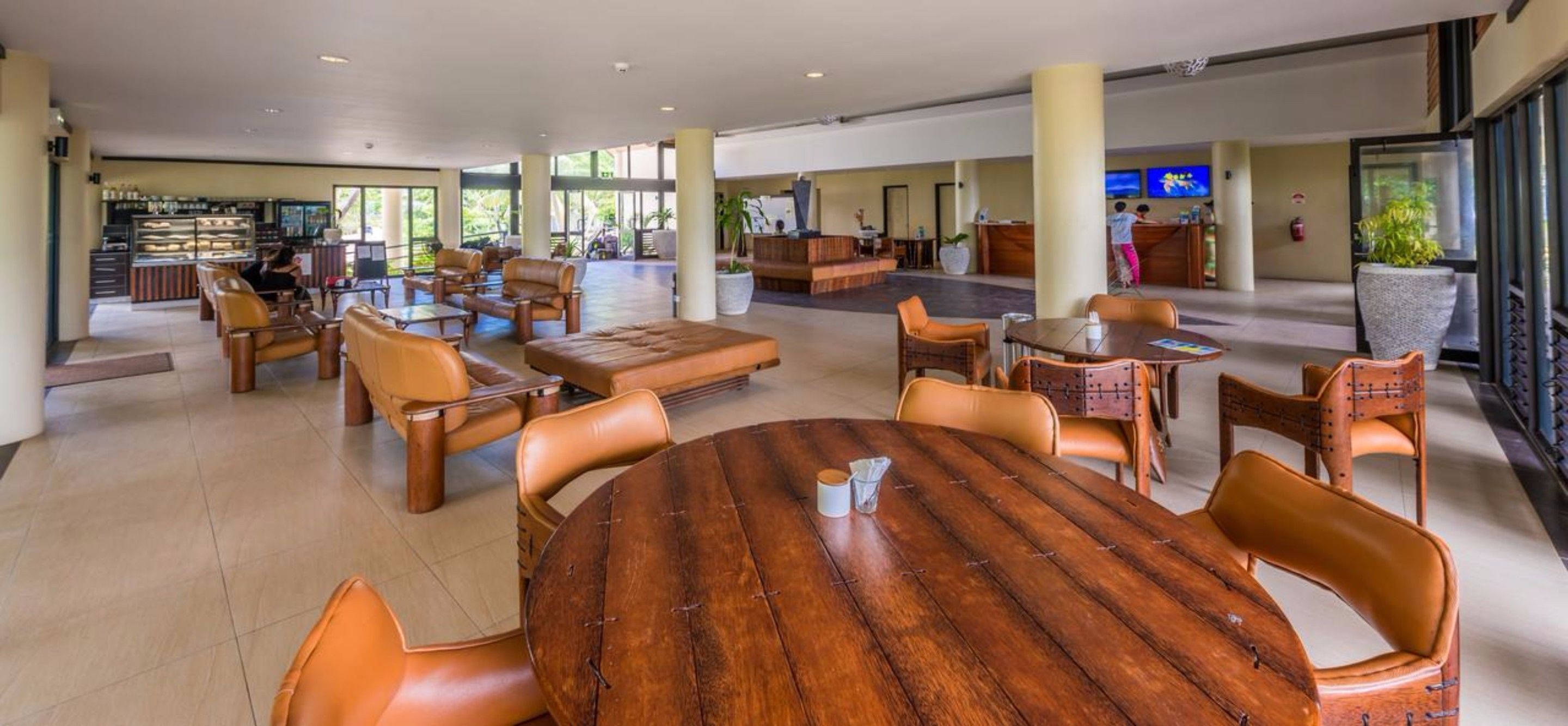 A spacious lobby with leather seating, a central wooden table, and a reception area with a TV.