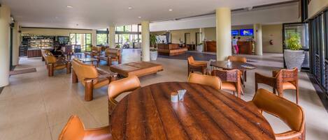 A spacious lobby with leather seating, a central wooden table, and a reception area with a TV.