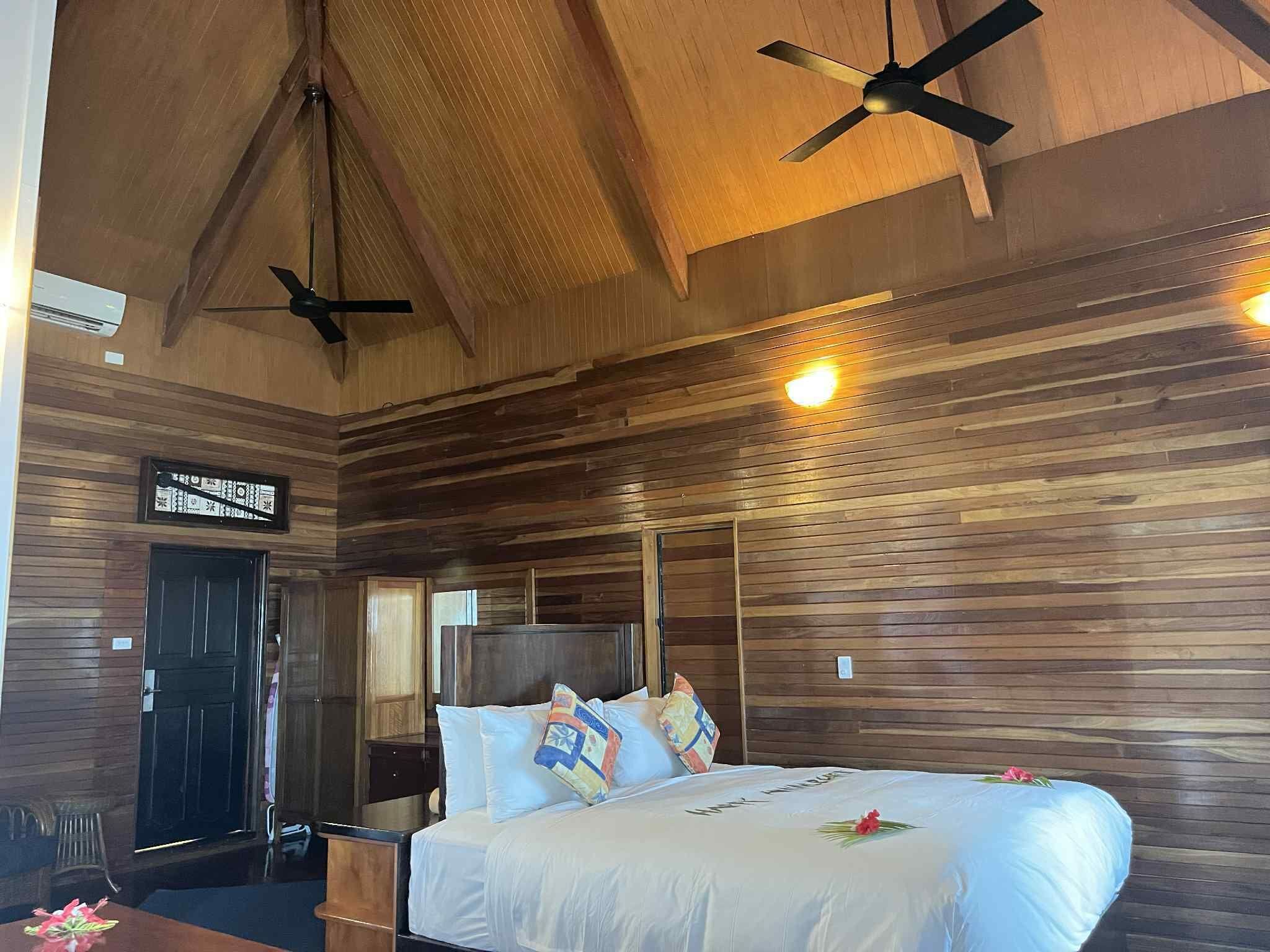 Habitación con paneles de madera, una cama, ventiladores de techo y un reloj en la pared.