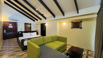 Una habitación de hotel con cama, un sofá verde, una mesita con una flor roja y un ventilador de techo.