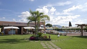 A hotel courtyard with outdoor seating, palm trees, and a swimming pool. - Al Canto delle Sirene (Terracina)