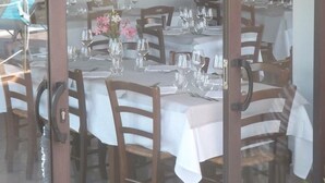 An outdoor dining area with tables set for two, wooden chairs, and wine bottles on shelves in the background. - Al Canto delle Sirene (Terracina)