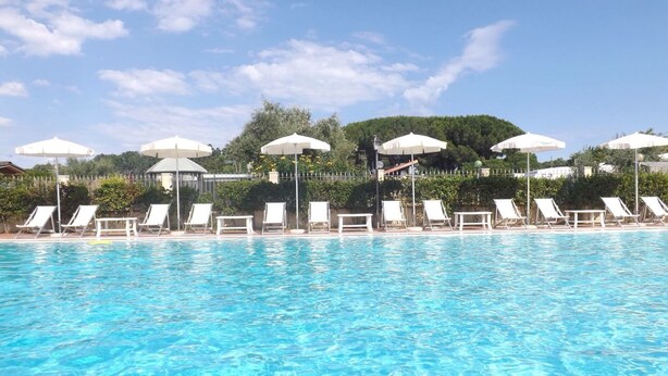 A swimming pool with white lounge chairs and umbrellas, surrounded by greenery and a clear sky. - Al Canto delle Sirene (Terracina)