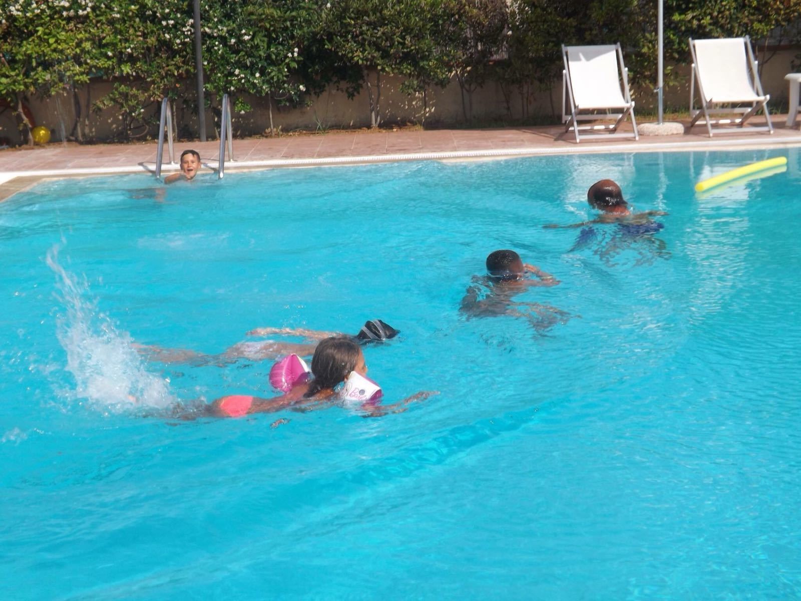 Una piscina con acqua cristallina circondata da una terrazza piastrellata e alberi.