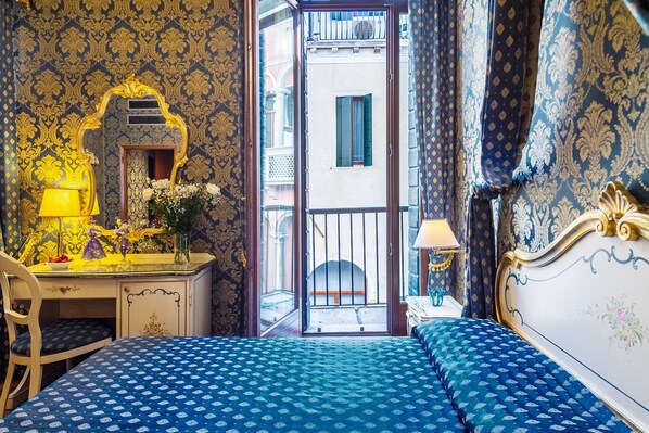A room with a bed, a desk, and a chair. There is a window with a view of the street.
