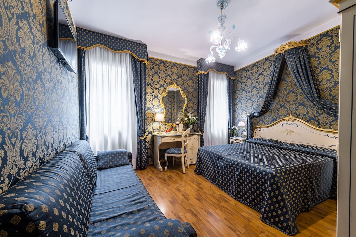 Ein Zimmer mit Holzboden, zwei Betten mit passendem blauem Bettzeug, einem Schreibtisch mit Stuhl, einem Spiegel und einer Chandelieber.