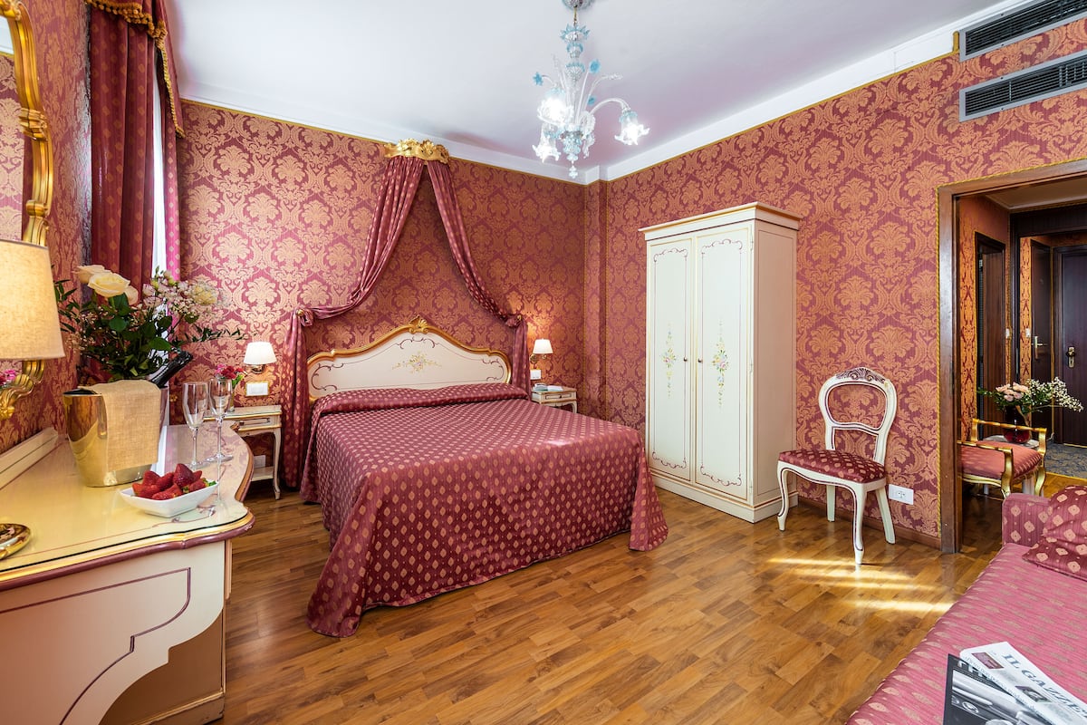 Ein Schlafzimmer mit einem großen Bett, einem Kleiderschrank, einem Schminktisch mit Spiegel und einer Deckenleuchte.