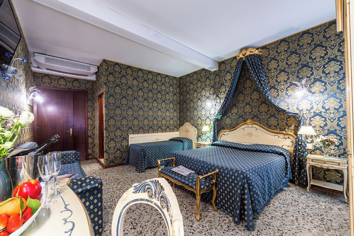 Ein Hotelzimmer mit zwei Betten, einem Schminktisch mit Spiegel, einem kleinen Tisch und einer Wandklimaanlage.