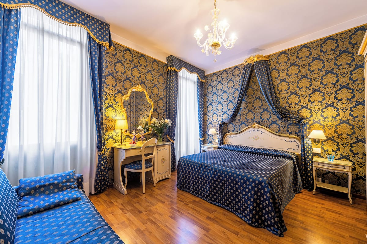Ein Zimmer mit einem Bett, einem Schreibtisch, einem Stuhl, einer Kommode und einer Kandelaber.