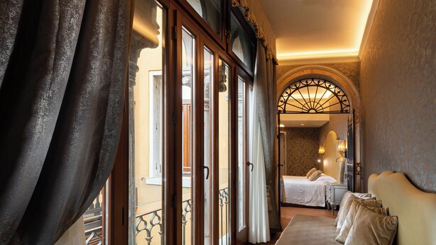 A hotel room with a large window, a balcony, and a bed with pillows. - Hotel Canaletto (Venice)