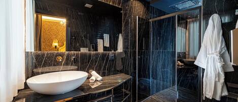 Une salle de bain moderne avec un grand lavabo blanc, des murs en marbre foncé et une douche séparée par des parois en verre.