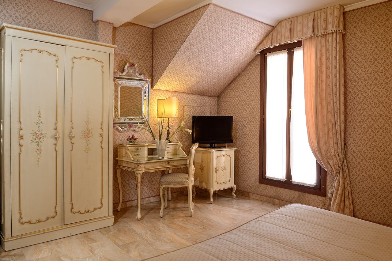 A bedroom with a large wardrobe, a desk with a mirror, a television, and a window with curtains.