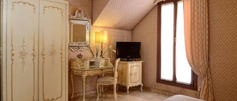 A bedroom with a large wardrobe, a desk with a mirror, a television, and a window with curtains.