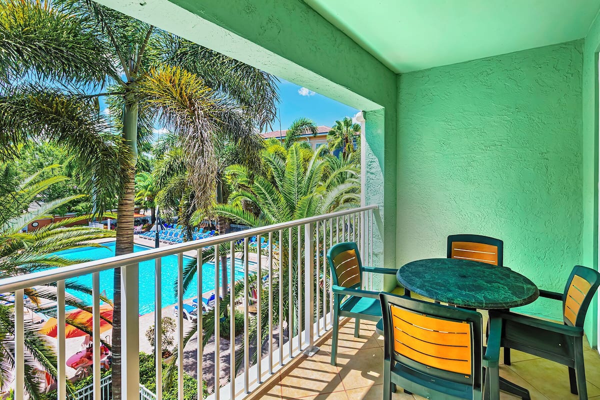 A balcony with a view of a swimming pool, surrounded by palm trees and lounge chairs.