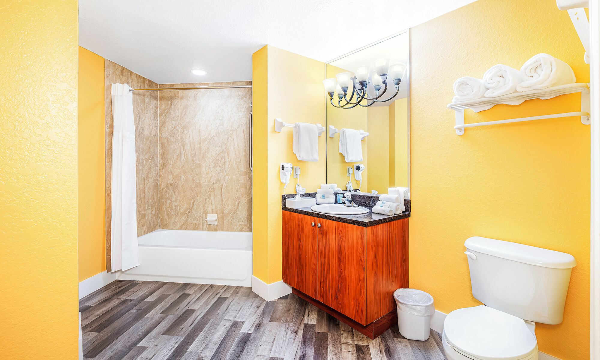 A bathroom with a wooden vanity, a white toilet, a shower area, and a mirror with towel hooks.