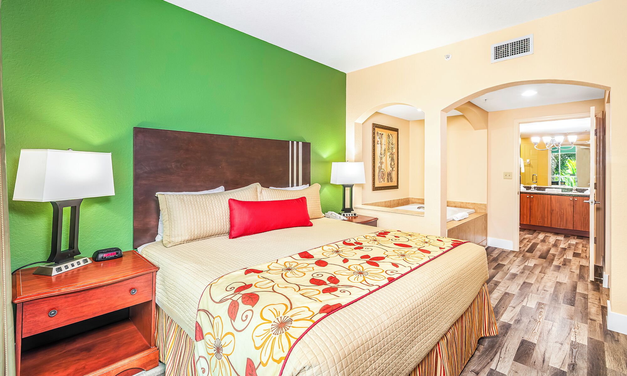 Une chambre d’hôtel avec un grand lit, deux tables de chevet, une commode, un miroir et une vue sur la salle de bain.