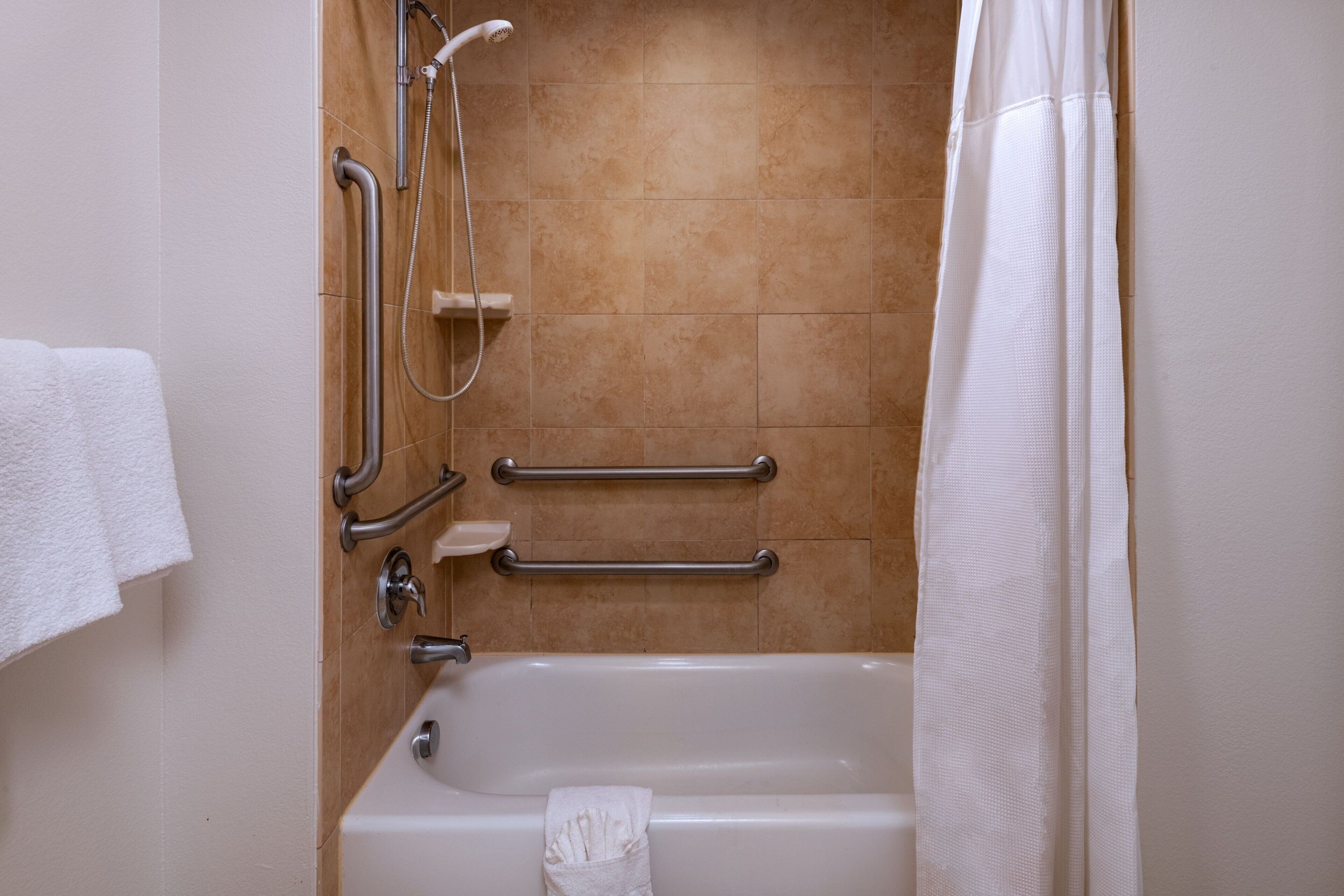 Un baño con bañera, barras de apoyo, cabezal de ducha y un perchero.