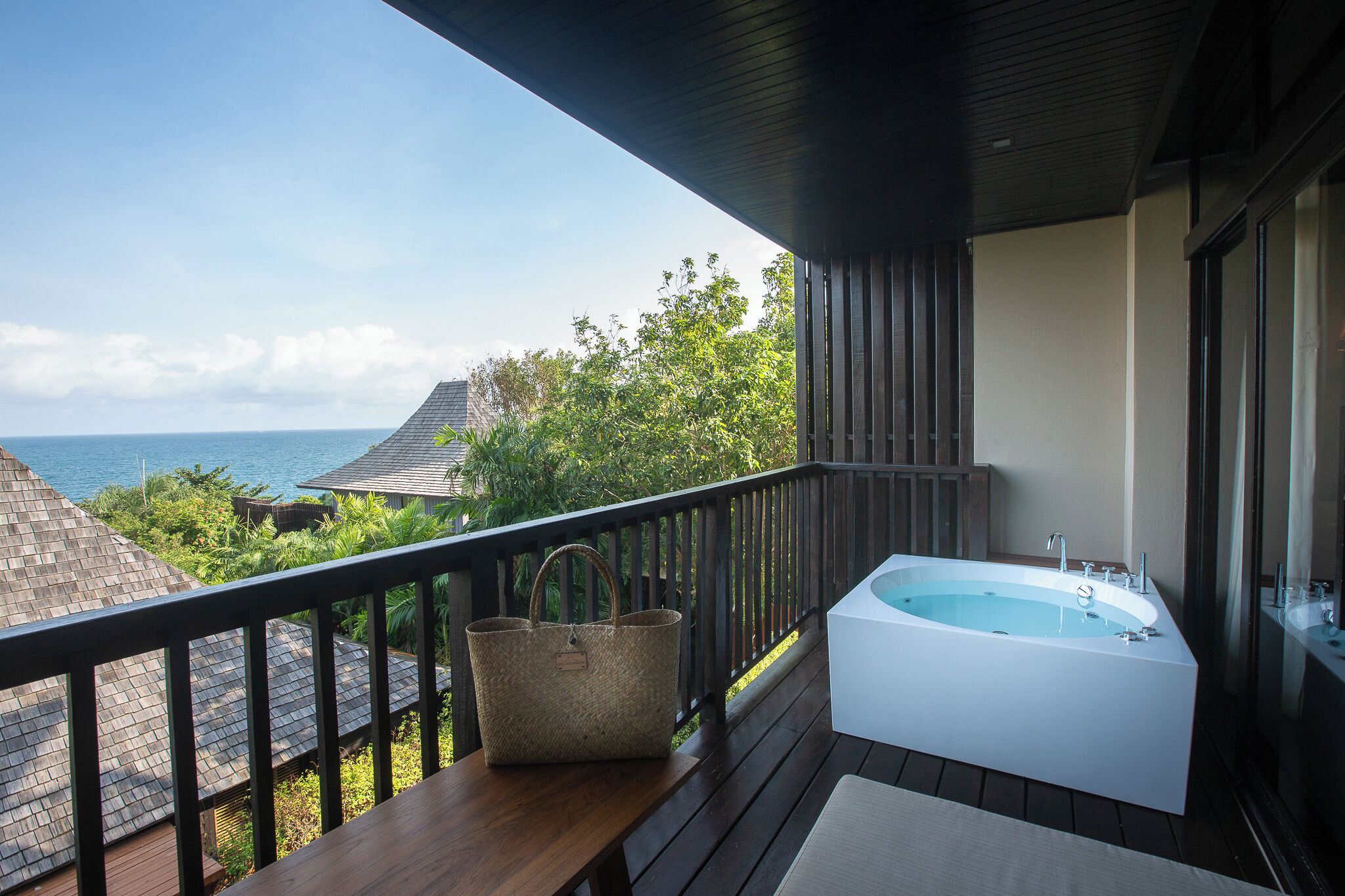 A balcony with a wooden deck, a white bathtub, and a woven basket.