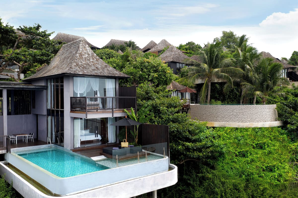 A modern villa with a pool, a balcony, and lush greenery.