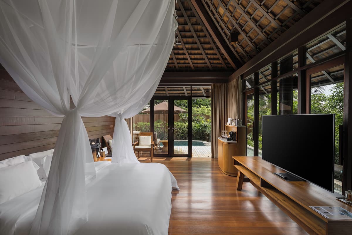 A bedroom with a canopy bed, a TV, and a wooden bench.