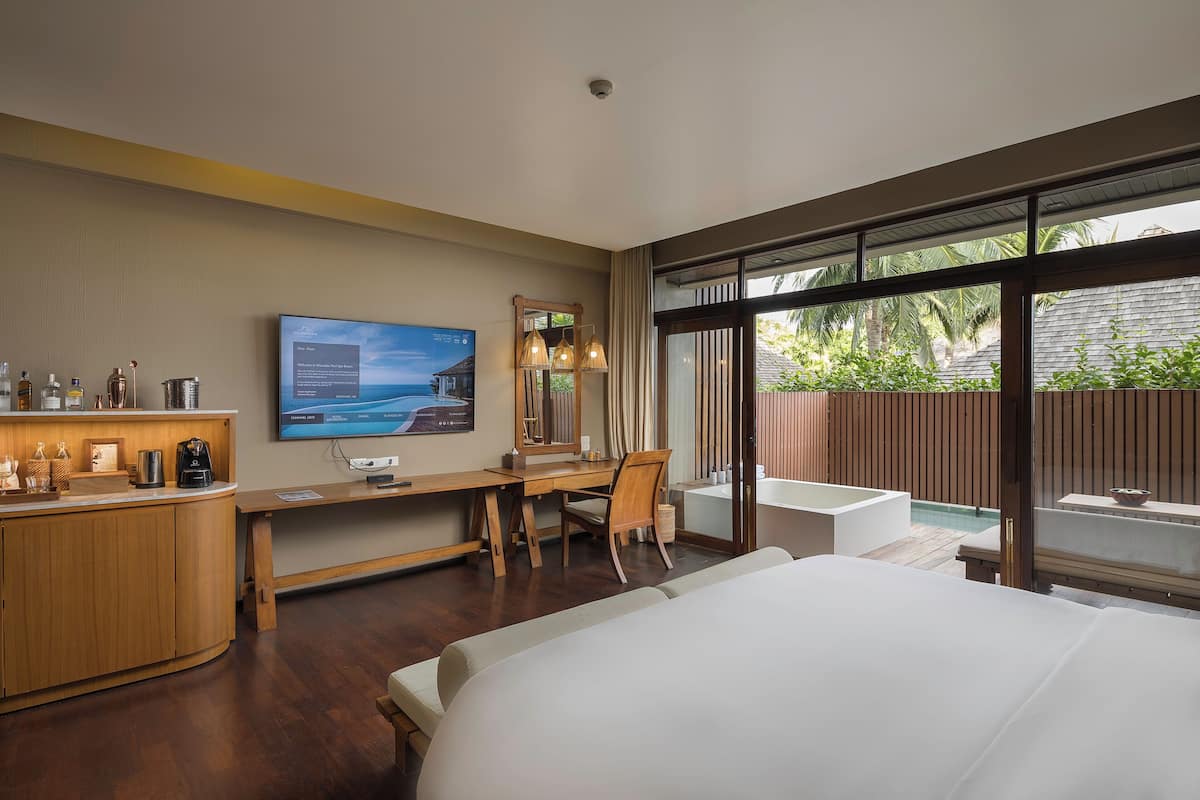 A hotel room with a bed, desk, chair, and a large window with a view of greenery and a pool.