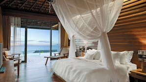 A bedroom with a large bed, a wooden headboard, a nightstand, a bedside table, and a view of the ocean through large windows. - Silavadee Pool Spa Resort (Koh Samui)