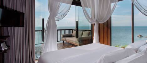 A bedroom with a large bed, a TV, and a balcony with a view of the sea.