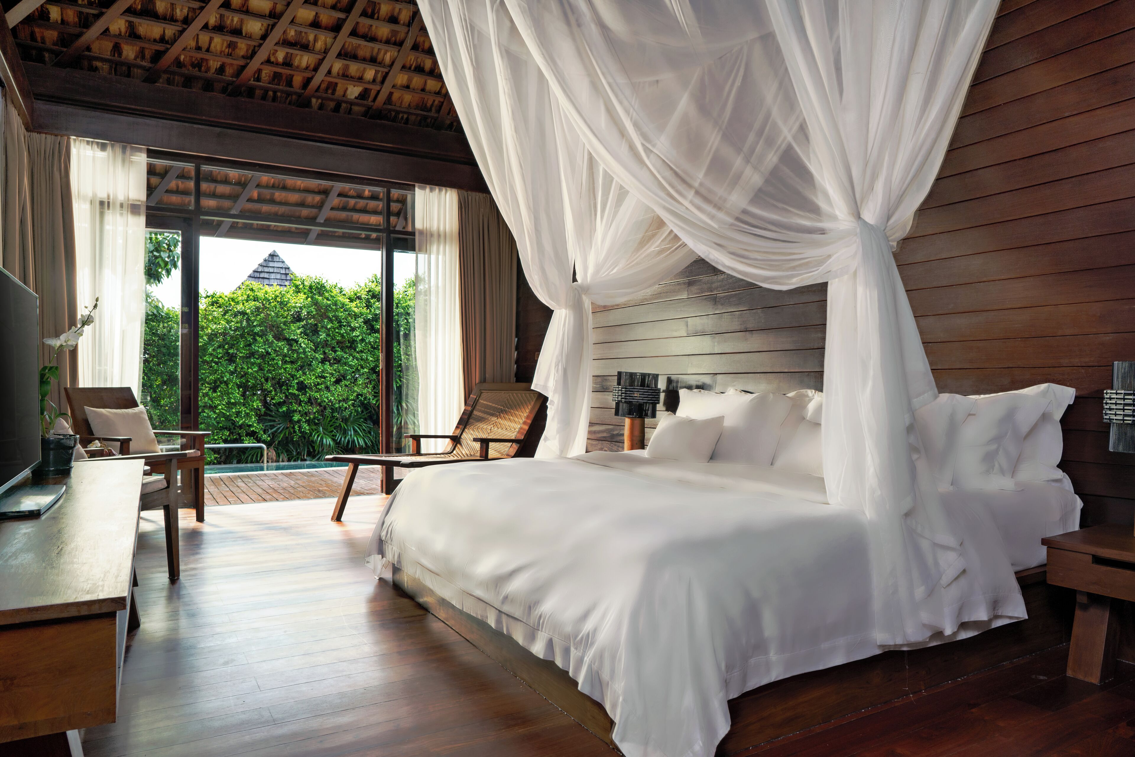 A spacious bedroom with a large bed, wooden flooring, a wooden headboard, and a canopy bed.