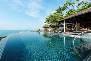 A infinity pool with a clear view of the sea, outdoor seating, and a covered area with umbrellas. - Silavadee Pool Spa Resort (Koh Samui)