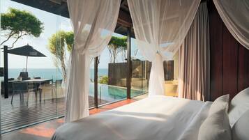 A bedroom with a large bed, white curtains, and a view of a pool and ocean.