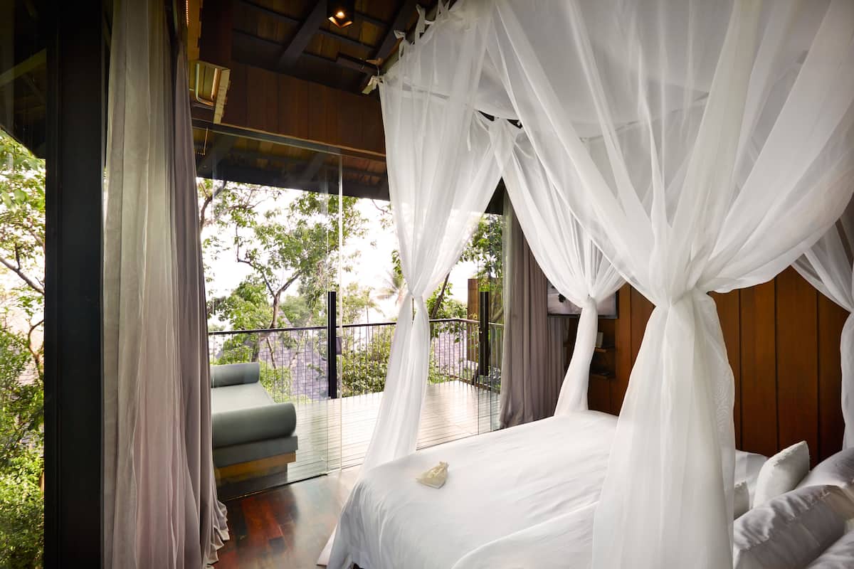 A bedroom with a canopy bed, a balcony with a sofa, and a view of trees.