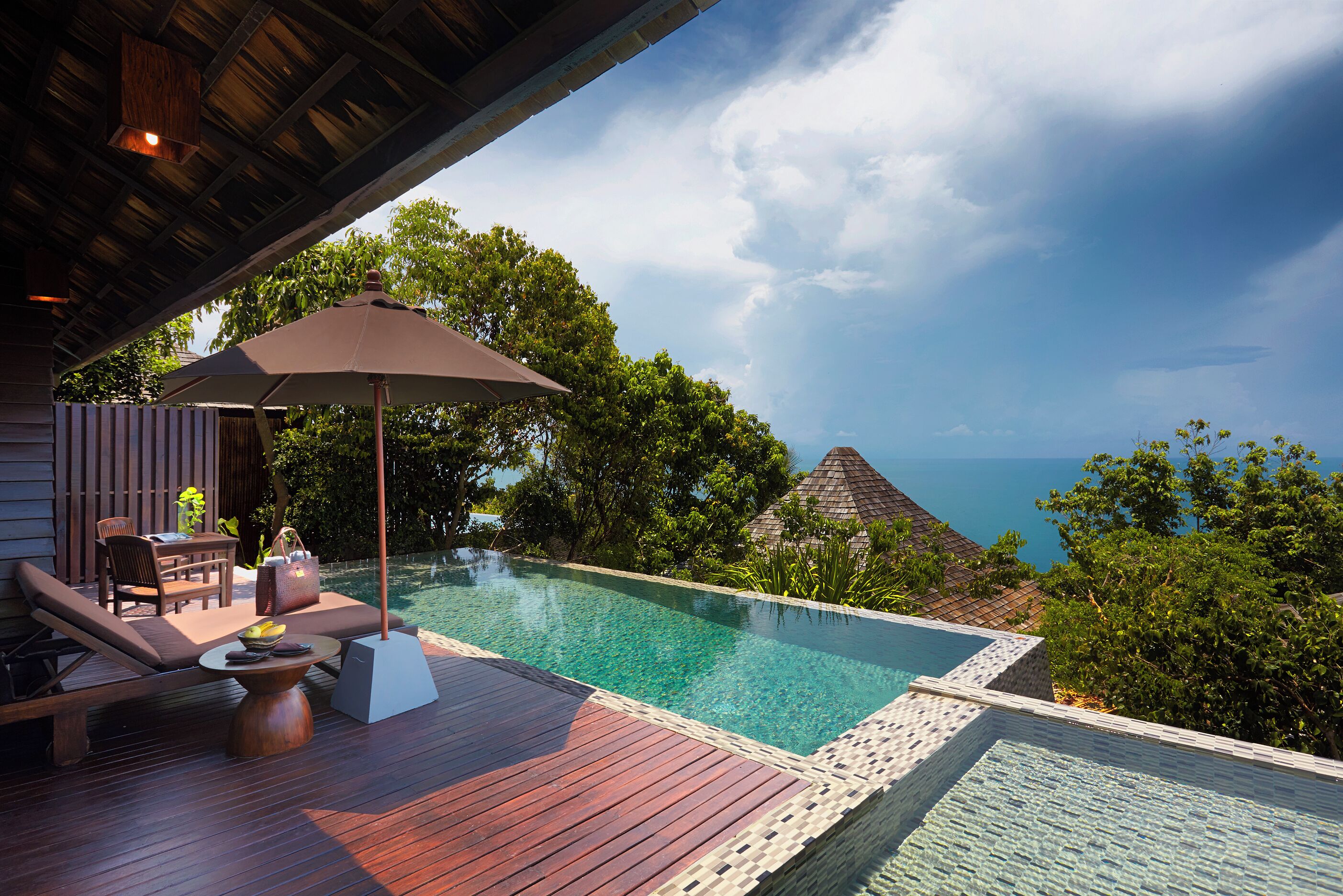 A wooden deck with a pool, lounge chairs, and an umbrella.