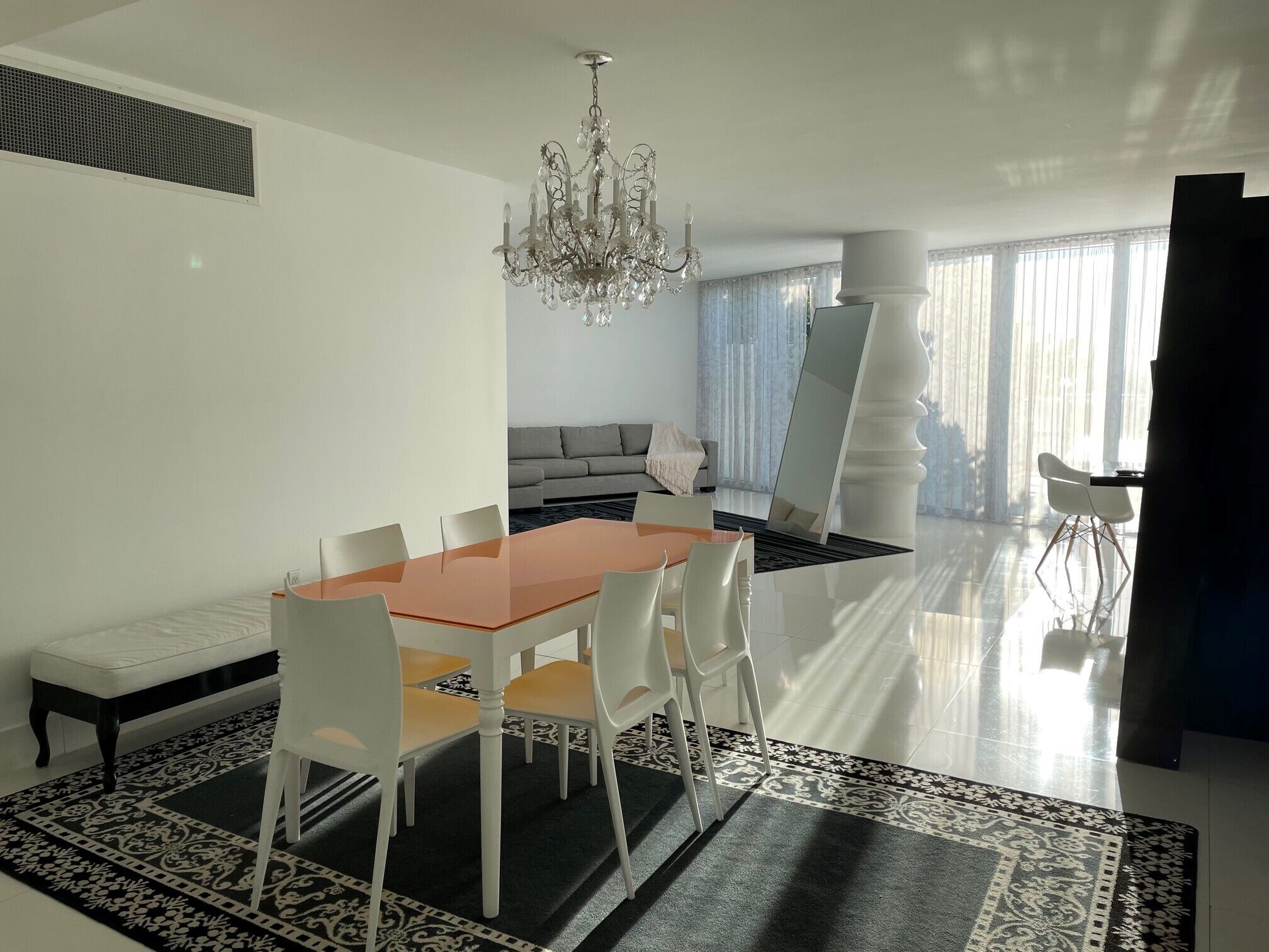 A modern dining area with a glass table, white chairs, and a chandelier.