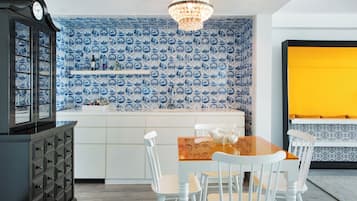 A kitchen with blue and white patterned tiles, a wooden dining table with white chairs, a chandelier, and a yellow accent wall.