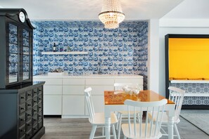 A kitchen with blue and white patterned tiles, a wooden dining table with white chairs, a chandelier, and a yellow accent wall.