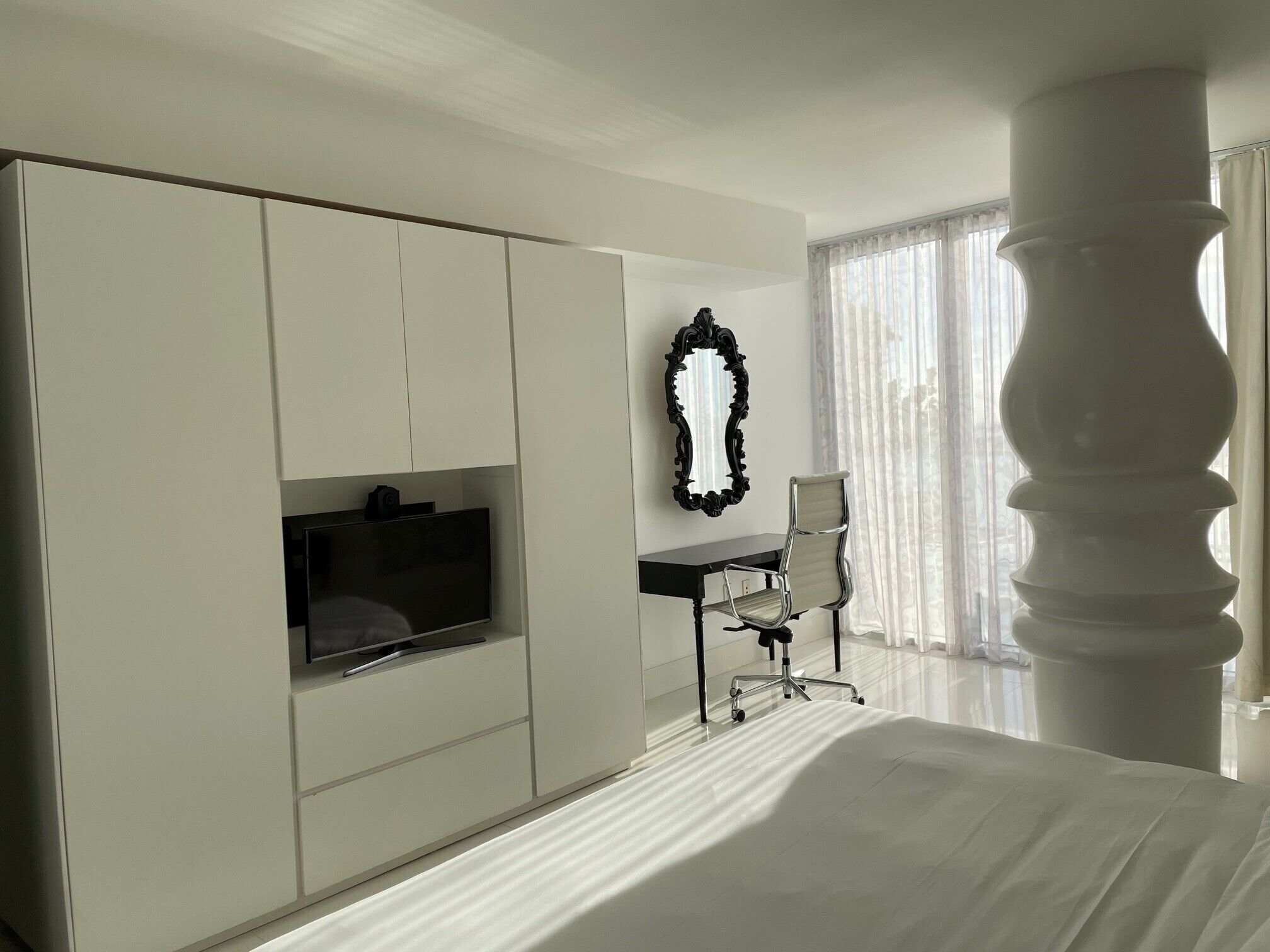 A hotel room with a large wardrobe, a desk with a chair, a television, and a large window with curtains.