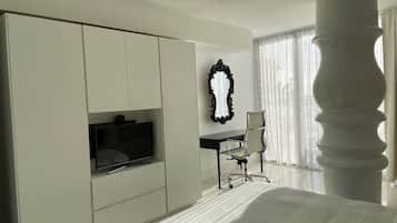 A hotel room with a large wardrobe, a desk with a chair, a television, and a large window with curtains.
