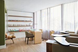 A modern, well-lit room with a wooden desk, chairs, and shelves with toiletries.