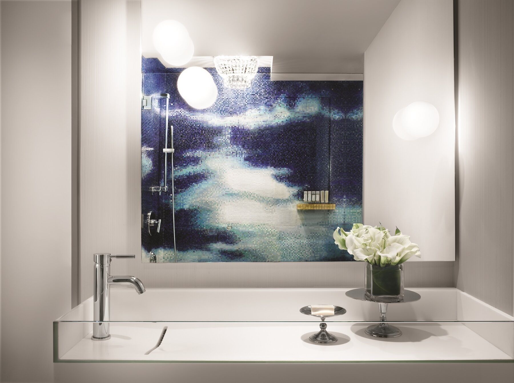 A modern bathroom with a large mirror, a glass sink, and a decorative vase with flowers.