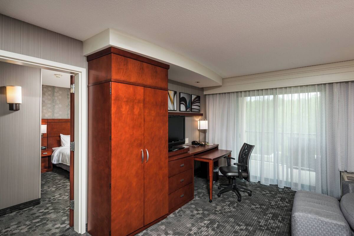 A hotel room with a large wooden wardrobe, a desk with a chair, a television, and a bed.