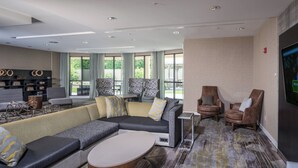 A modern hotel lobby with a sectional sofa, armchairs, a small table, and a flat-screen TV on the wall. - Courtyard by Marriott Bangor (Bangor)