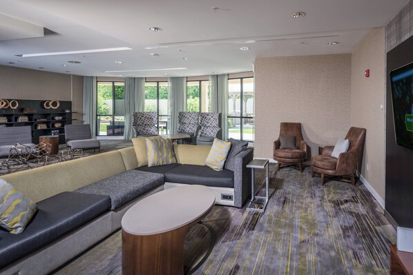 A modern hotel lobby with a sectional sofa, armchairs, a small table, and a flat-screen TV on the wall. - Courtyard by Marriott Bangor (Bangor)