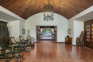A spacious lobby with a high arched ceiling, a central chandelier, and a view of a garden through an archway.