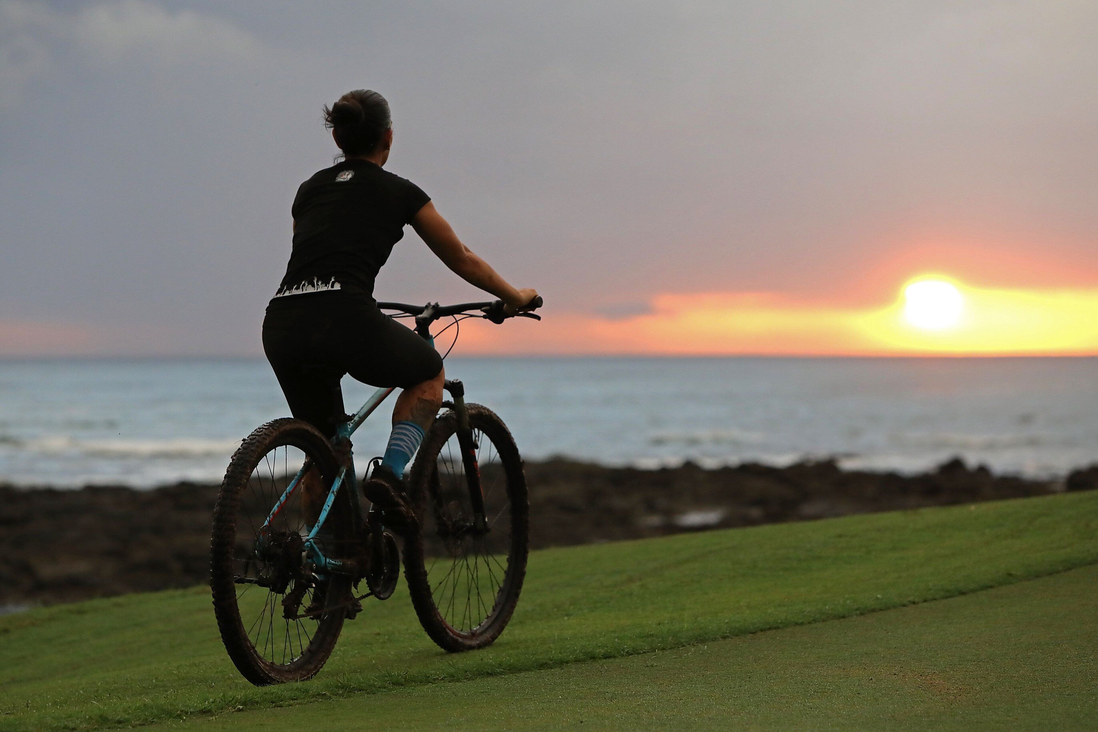 Una persona montando en bicicleta por un sendero cubierto de césped, con un atardecer de fondo.
