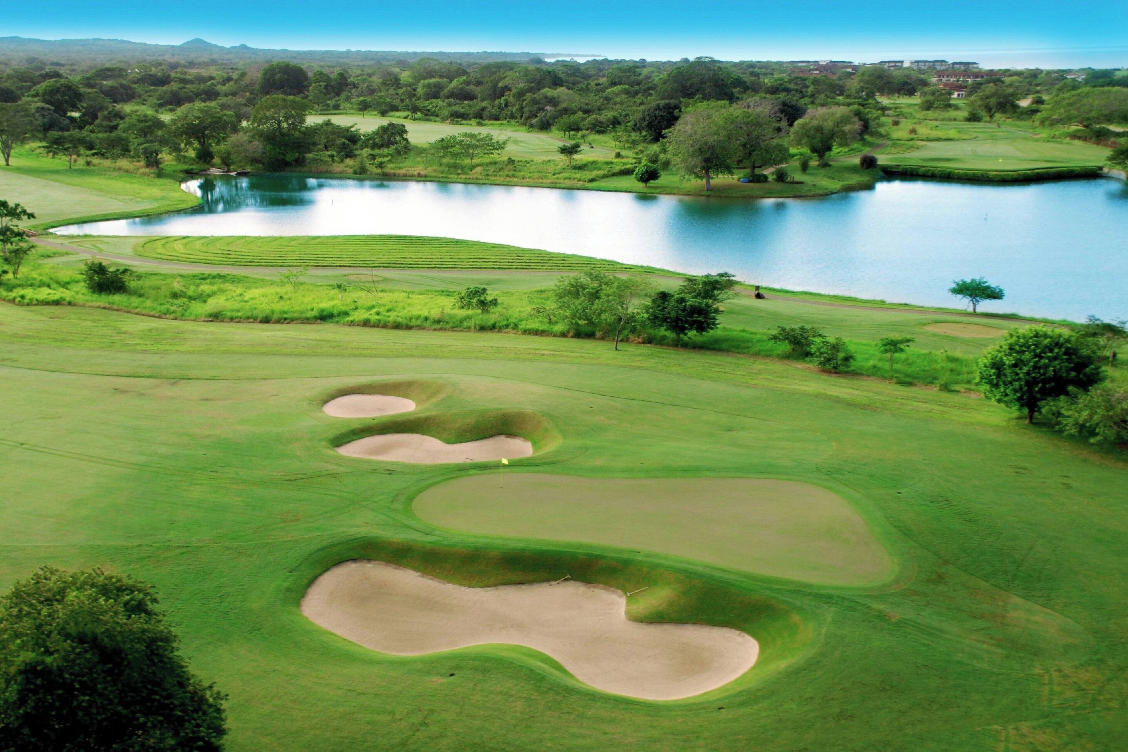 Ein Golfplatz mit Sandbunkern, einem Teich und umgebender Grünfläche.