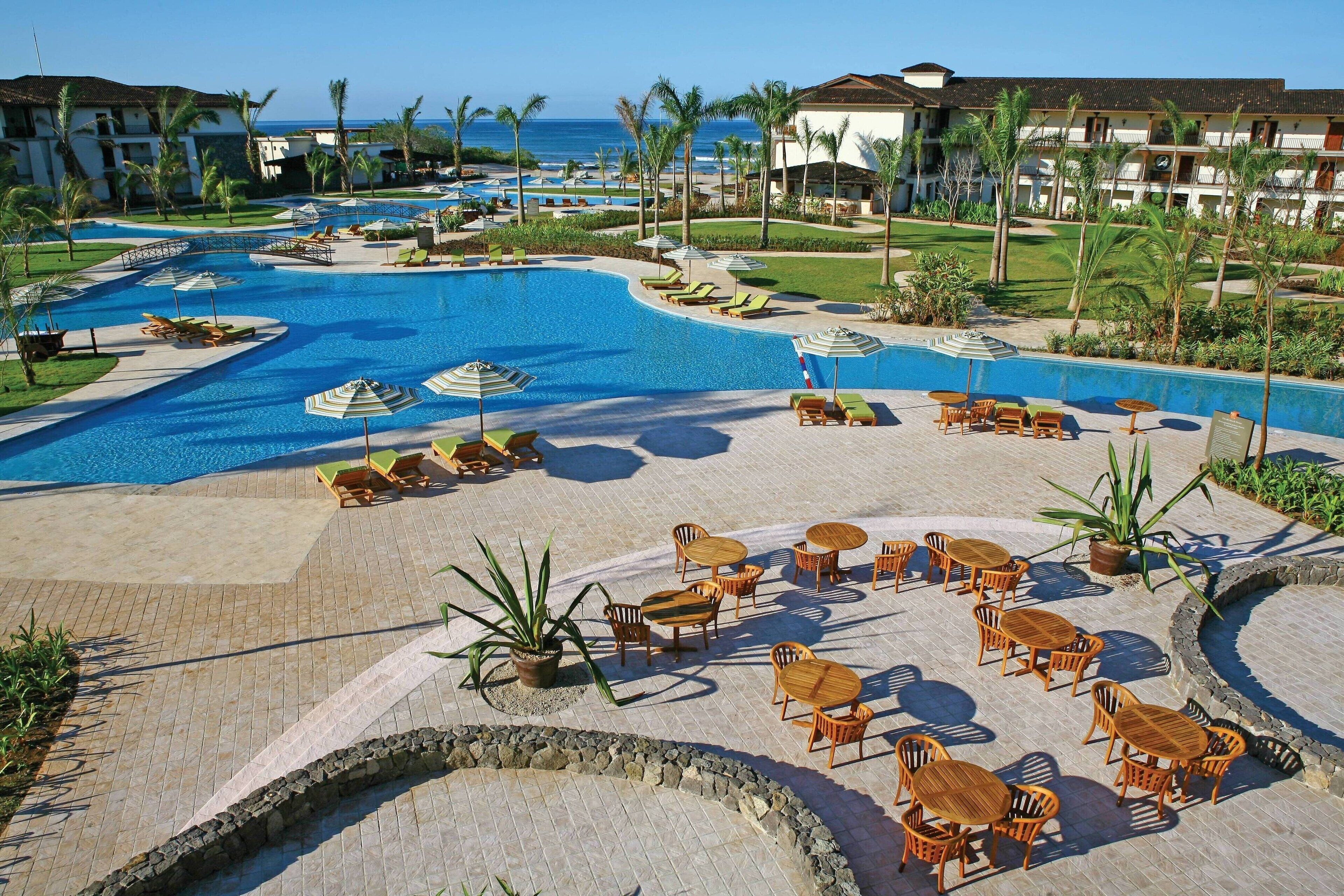 A resort pool area with lounge chairs, umbrellas, and a view of the ocean.