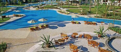 A resort pool area with lounge chairs, umbrellas, and a view of the ocean.