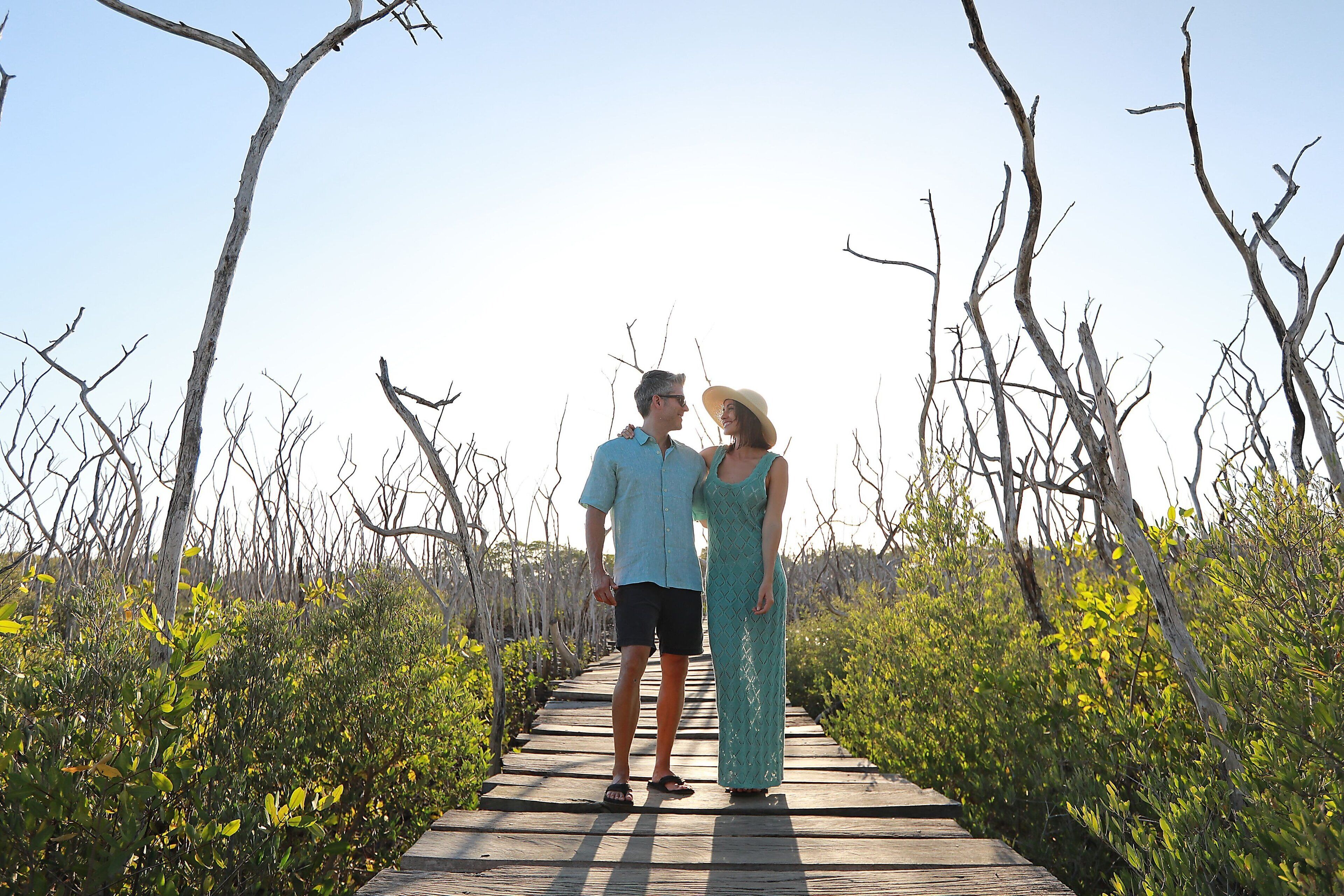 Un couple se tient sur une promenade en bois, entouré de verdure.