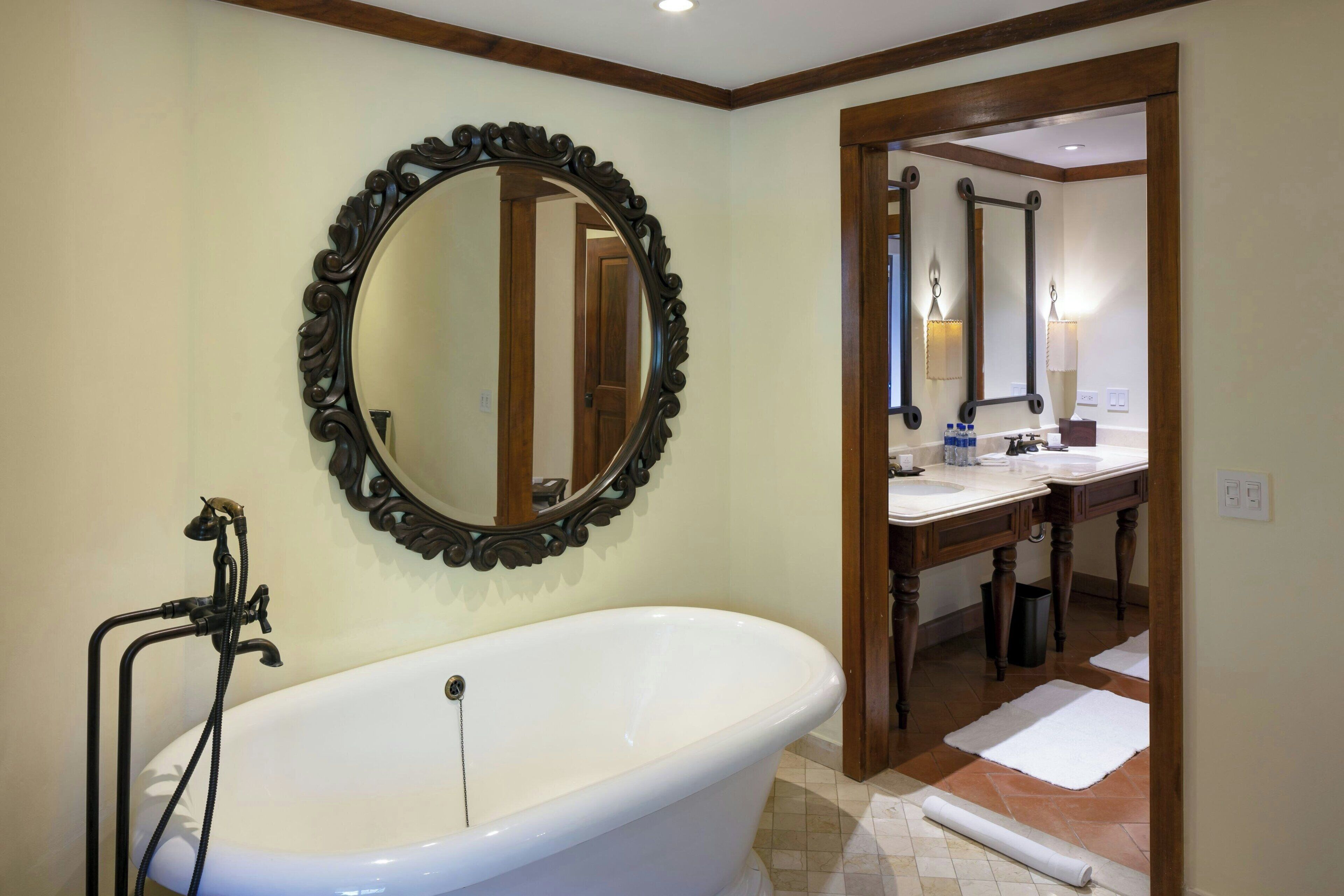 Un baño con una bañera independiente, un espejo grande y ornamentado, y un tocador de madera con lavabo.