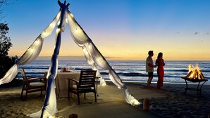 A beachside dining setup with a table and chairs, a fire pit, and a tent-like structure with draped fabric. - JW Marriott Guanacaste Resort & Spa (Tamarindo)